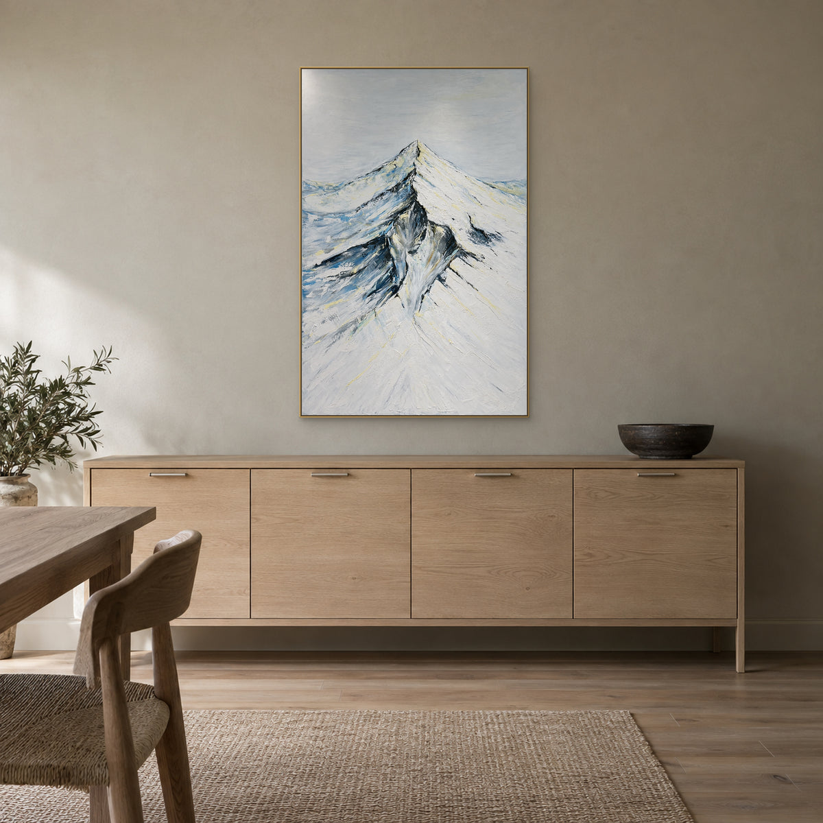 Tableau de montagne enneigée dans un cadre champagne au-dessus d'un buffet en bois clair