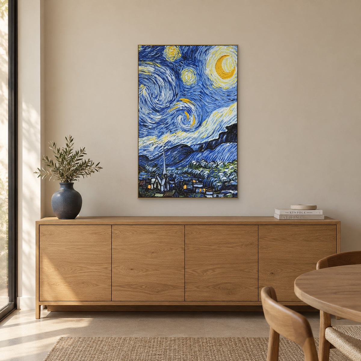 Village sous les étoiles dans un cadre champagne, au-dessus d’un buffet aspect chêne avec un vase bleu-gris, des rameaux et des livres.