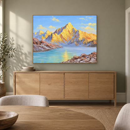 Golden mountain lake painting in a champagne-tone frame above a pale wood dining-room sideboard