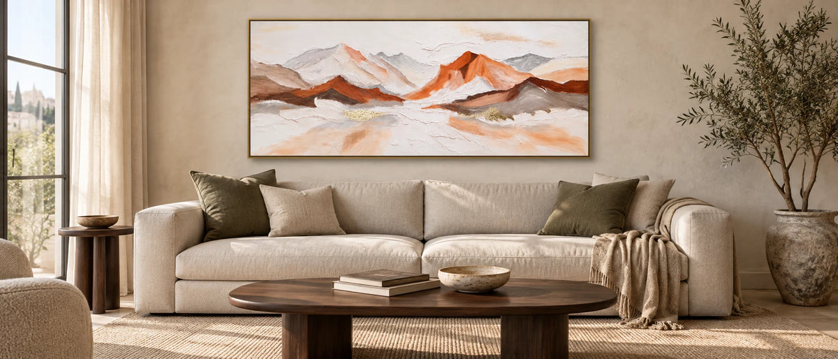 Tableau de montagnes cuivrées et ivoire dans un cadre doré, au-dessus d’un canapé en lin, avec table basse en noyer, tapis tissé et lumière naturelle.