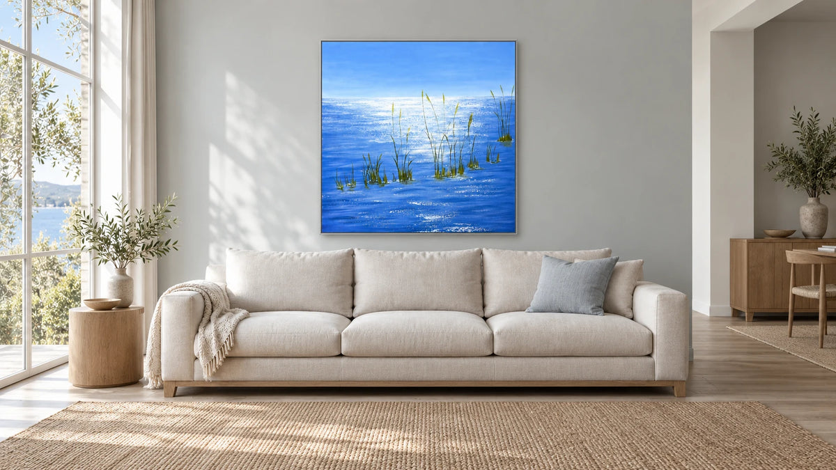 Silver Light on Blue Water in a slim silver frame above an ivory sofa, in a light-filled room