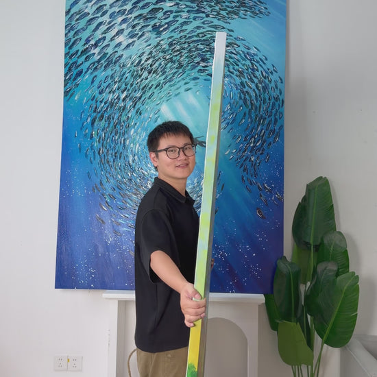 Studio video turning the tall painting from its side to reveal a blue lake, pink flowers, yellow-green trees and a small bear